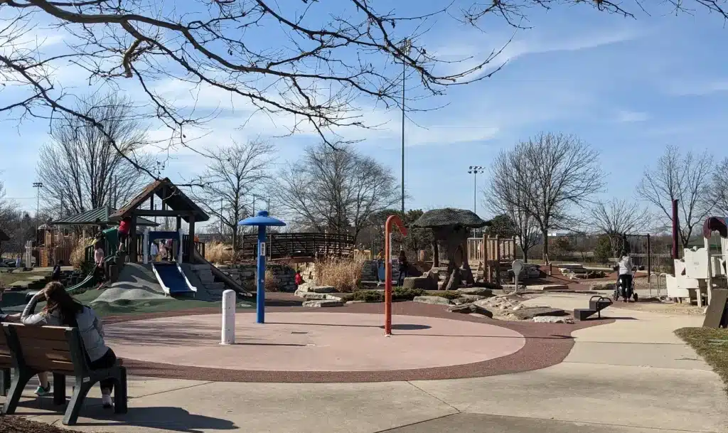 Children playing at a nature-themed playground with splash pad and climbing structures at a public park in Burr Ridge, IL